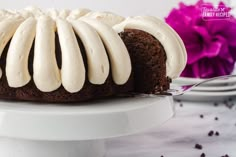 a bundt cake with white frosting on a plate next to a purple flower