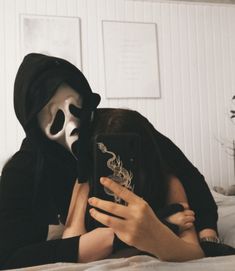 a woman wearing a mask and holding a cell phone in front of her face while laying on a bed