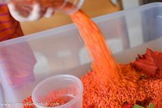 a person pouring orange liquid into a container filled with red and green sprinkles