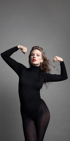 a woman in black bodysuit posing with her arms behind her head and hands on her hips