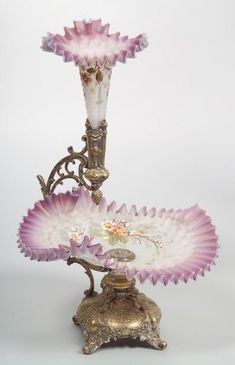 an ornate pink and white glass vase sitting on top of a stand with two candles