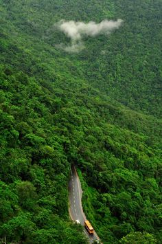 the road is surrounded by lush green hills and trees, with a train on it's side