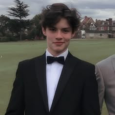 two young men in tuxedos standing next to each other on a golf course