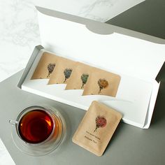 a cup of tea sitting next to an open box with four small cards in it