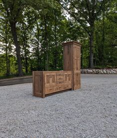 a wooden bench sitting in the middle of a gravel covered parking lot next to trees