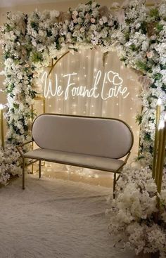 a white couch sitting under a wedding arch with flowers and lights on it's sides