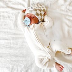 a baby is sleeping with a pacifier in it's mouth and wearing a checkered hat