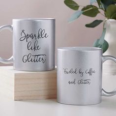 two silver coffee mugs sitting on top of a wooden block