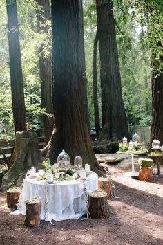 an outdoor table set up in the middle of a forest with candles and flowers on it