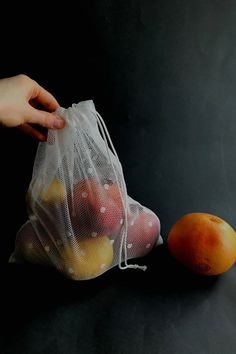 a hand holding a mesh produce bag next to an orange on a table with the words reusable mesh produce bags