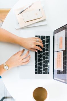 a woman is typing on her laptop while sitting at a table with a cup of coffee