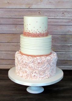 a three tiered wedding cake with white frosting and pink roses on the side