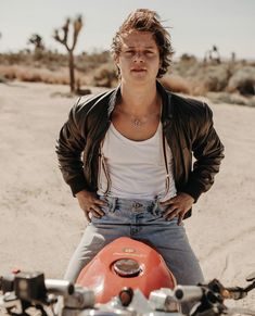 a man sitting on top of a motorcycle in the desert with his hands on his hips