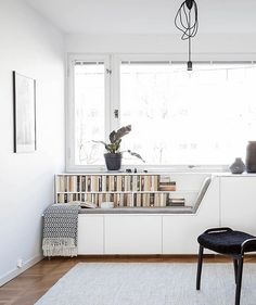 a living room with white furniture and bookshelves on the wall next to a window