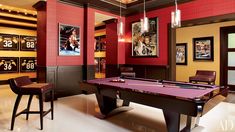 a billiard table in a room with red walls and lights hanging from the ceiling