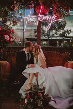 a bride and groom sitting on a couch in front of a neon sign