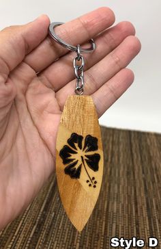 a hand holding a wooden keychain with a black flower design on it's side