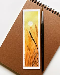 a watercolor painting on paper with a pen next to it and a notepad