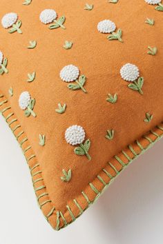 an orange pillow with white flowers and green leaves on the front, sitting on a white surface