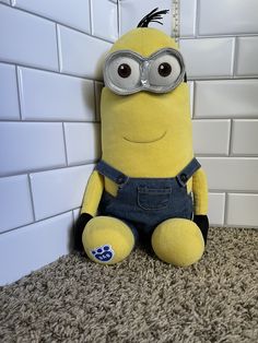 a yellow stuffed animal sitting on top of a carpet next to a white tiled wall