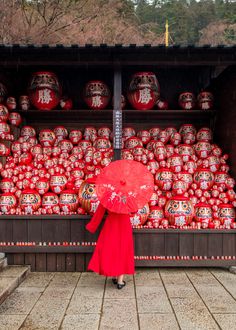 a woman in a red dress holding an umbrella next to a large amount of red vases