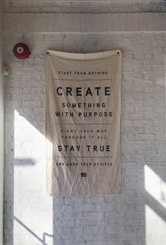 a white brick wall with a sign hanging from it's side that says create something with purpose