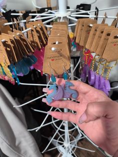 a person holding up small elephant shaped earrings in front of a rack with tags on them