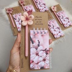 a hand holding a notepad with pink flowers on it next to four notebooks