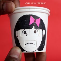 a hand holding a coffee cup with a face painted on the side and a pink bow