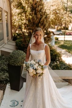 a woman in a wedding dress is standing on the steps holding a bouquet and smiling at the camera