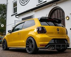 the rear end of a yellow car parked in front of a white building with black rims