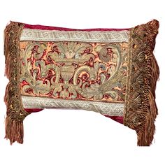 an embroidered pillow with fringes and tassels on the sides, sitting against a white background