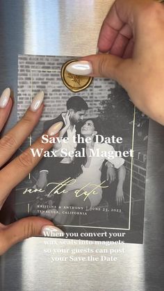 two hands holding a save the date card with a gold ring on top of it