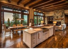 a large open concept kitchen and living room with wood flooring, windows, and stone fireplace