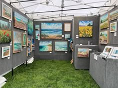 an art exhibit with paintings on the walls and green grass in the foreground, under a white tent