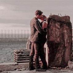 a man and woman standing next to each other near a large rock in the middle of a field