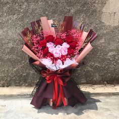 a bouquet of red and pink flowers in front of a stone wall with a ribbon tied around it