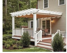 a white pergolan sitting on top of a wooden deck next to a house