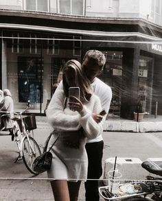 a man and woman are walking down the street looking at their cell phones while holding each other's hands