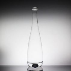 a clear glass bottle sitting on top of a reflective surface in front of a white wall