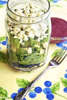 a glass jar filled with salad next to a fork and spoon on a floral table cloth