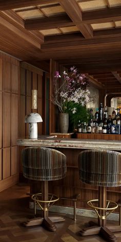 two stools in front of a bar with bottles on the counter and flowers behind it