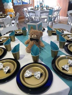 a teddy bear sitting on top of a blue and white table cloth with gold rimmed plates