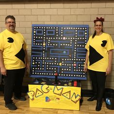 two people in matching yellow shirts standing next to a pac - man board game costume