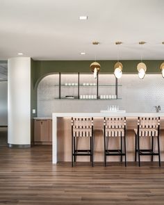 a kitchen with wooden flooring and white counter tops next to a bar area filled with stools