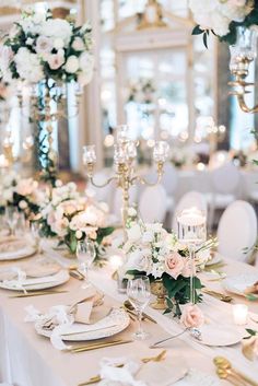 the table is set with white and pink flowers, candles, and place settings for dinner