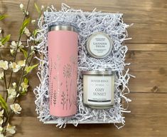 a pink travel mug and candle in a gift box with white flowers on a wooden table