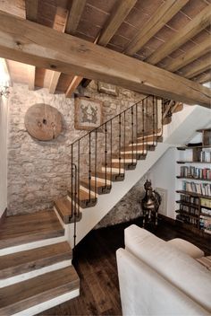 a living room filled with furniture next to a stone wall and wooden floored stairs