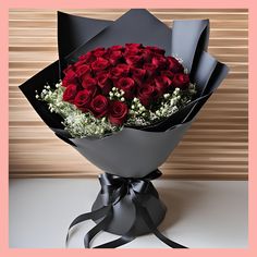 a large bouquet of red roses wrapped in black paper and tied with a satin ribbon