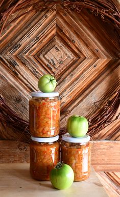 three jars filled with food sitting on top of a wooden table next to two green apples